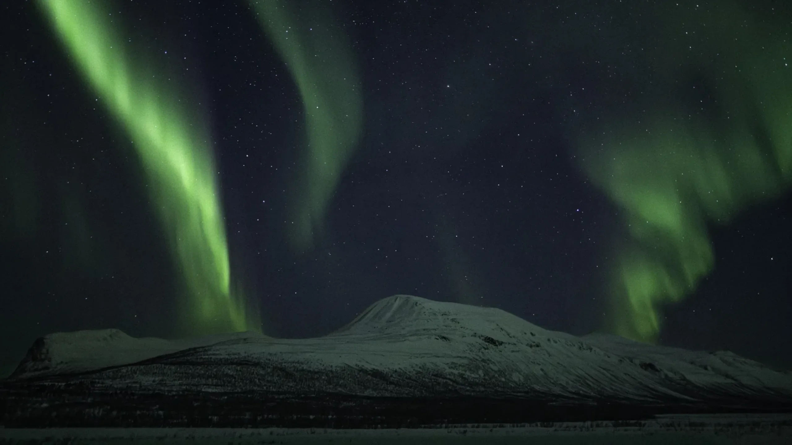 Northern lights over snow-covered mountains outside Kiruna, Swedish Lapland